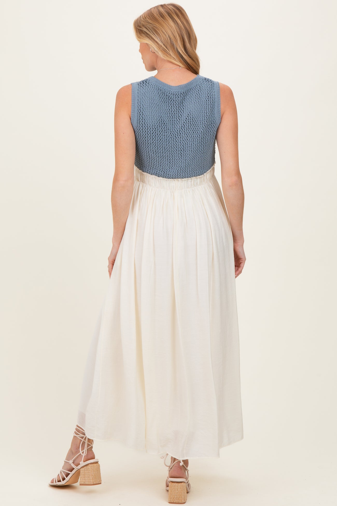 woman wearing a blue knitted maternity dress with a white skirt, showing a flowing design and back view