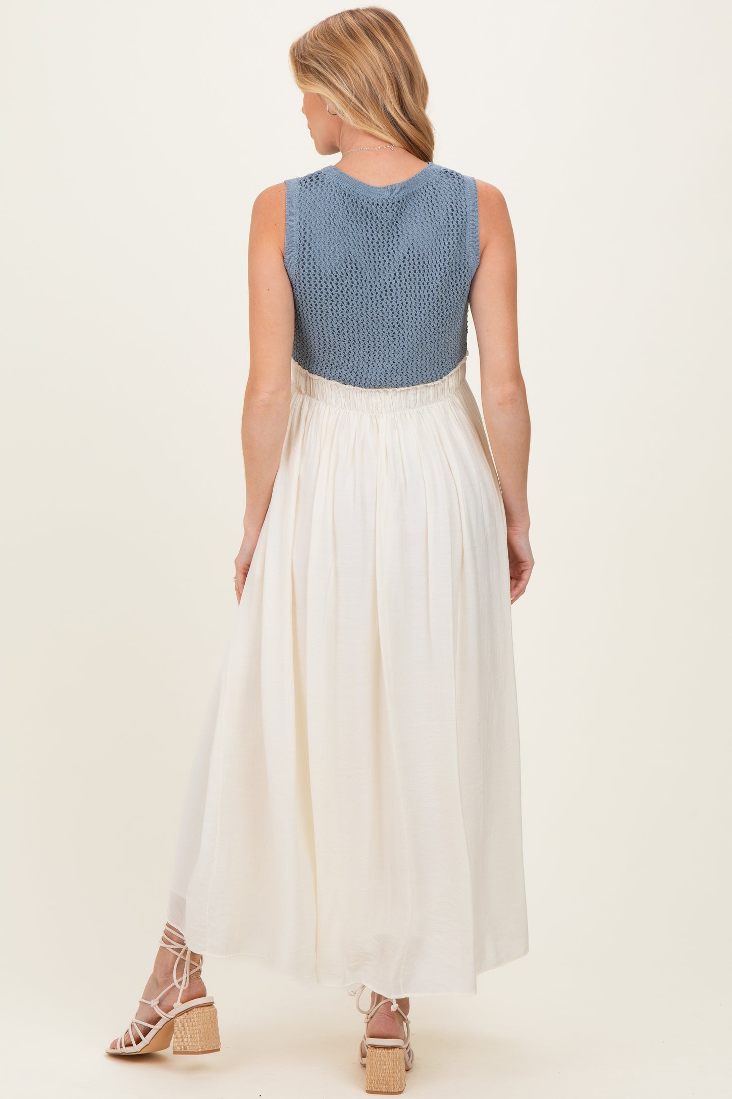 woman wearing a blue knitted maternity dress with a white skirt, showing a flowing design and back view