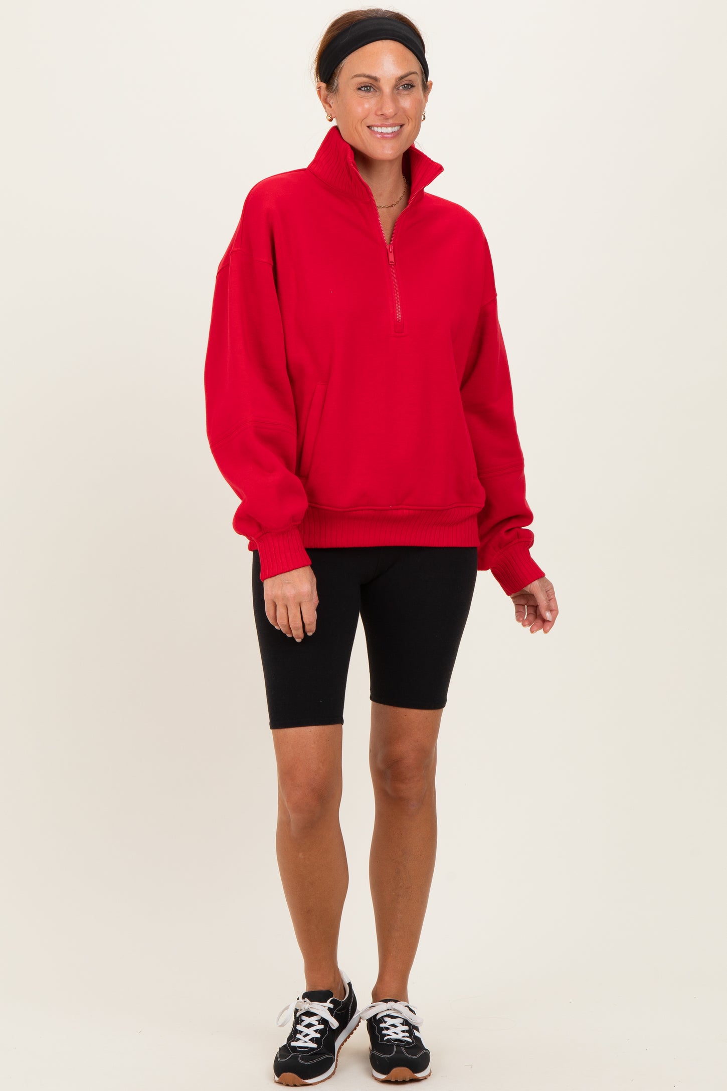 woman wearing a red quarter-zip pullover sweatshirt with black bike shorts and sneakers