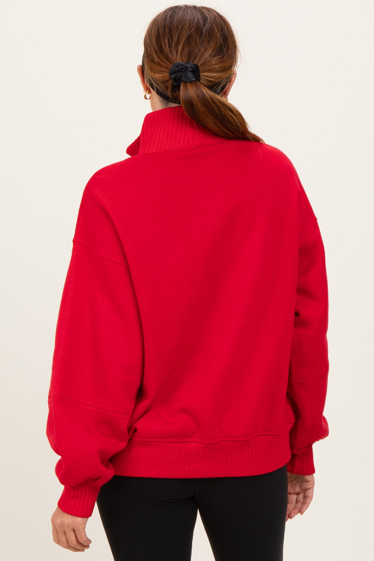 woman wearing a red oversized sweatshirt with a high collar and ribbed hem, viewed from the back