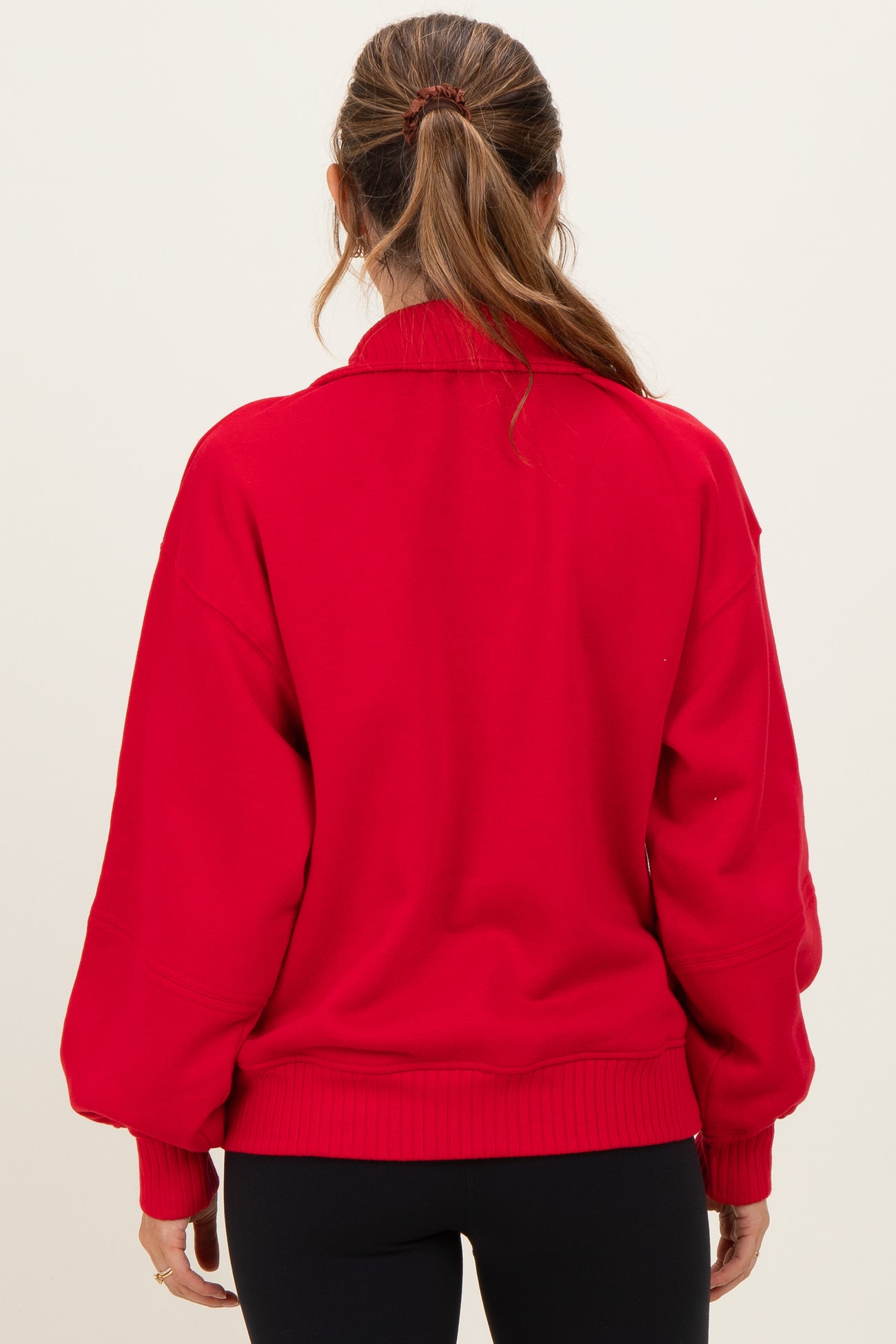 woman wearing a red oversized maternity sweatshirt, showing the back view and styled with relaxed sleeves