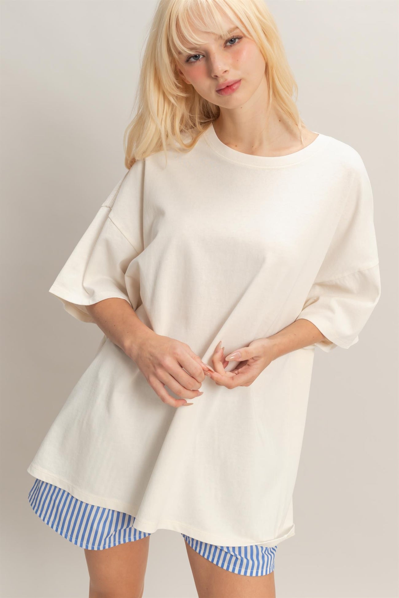 woman wearing a cream oversized t-shirt with short sleeves and styled with blue and white striped shorts