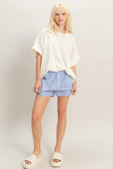 woman wearing a cream oversized t-shirt with rolled sleeves and blue striped shorts, paired with light sandals