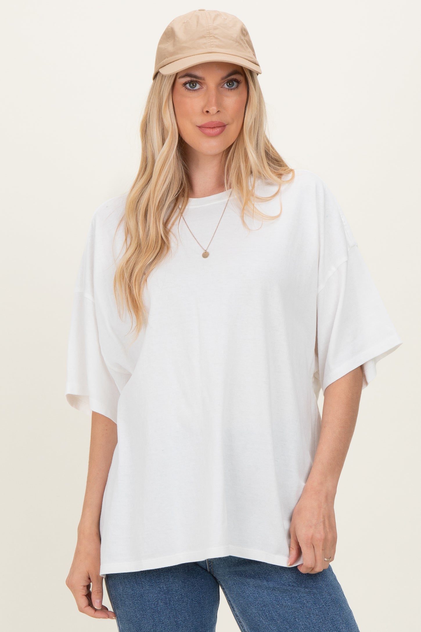 woman wearing an oversized white t-shirt with short sleeves and blue jeans, paired with a beige cap