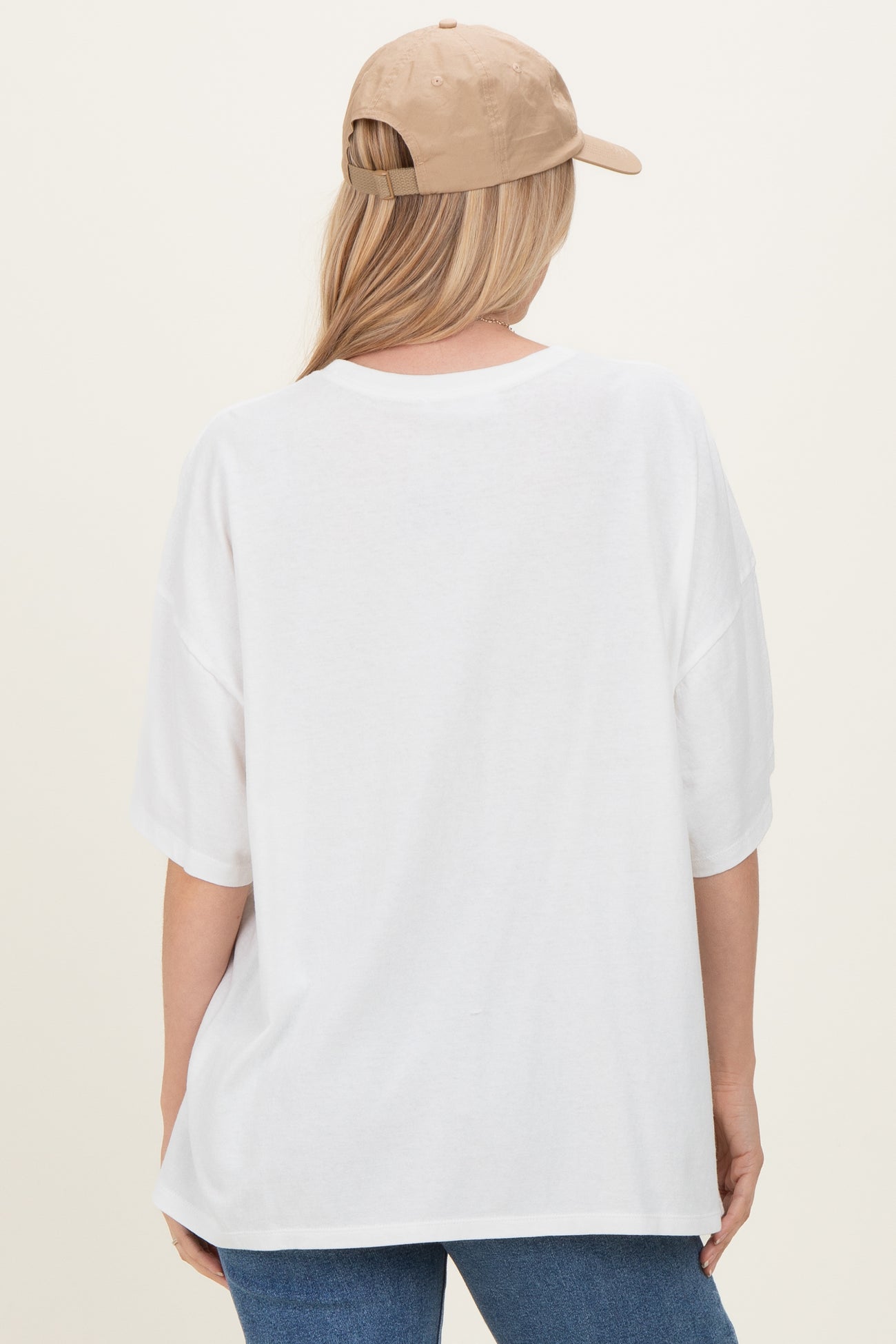 woman wearing a white oversized t-shirt and a beige baseball cap, viewed from the back