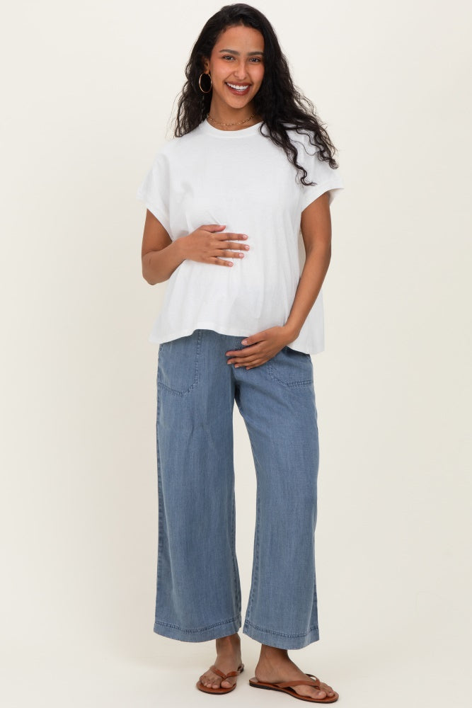 woman wearing a white maternity top and light blue wide-leg jeans, smiling and holding her baby bump