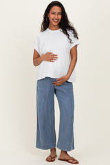 woman wearing a white maternity top and light blue wide-leg jeans, smiling and holding her baby bump
