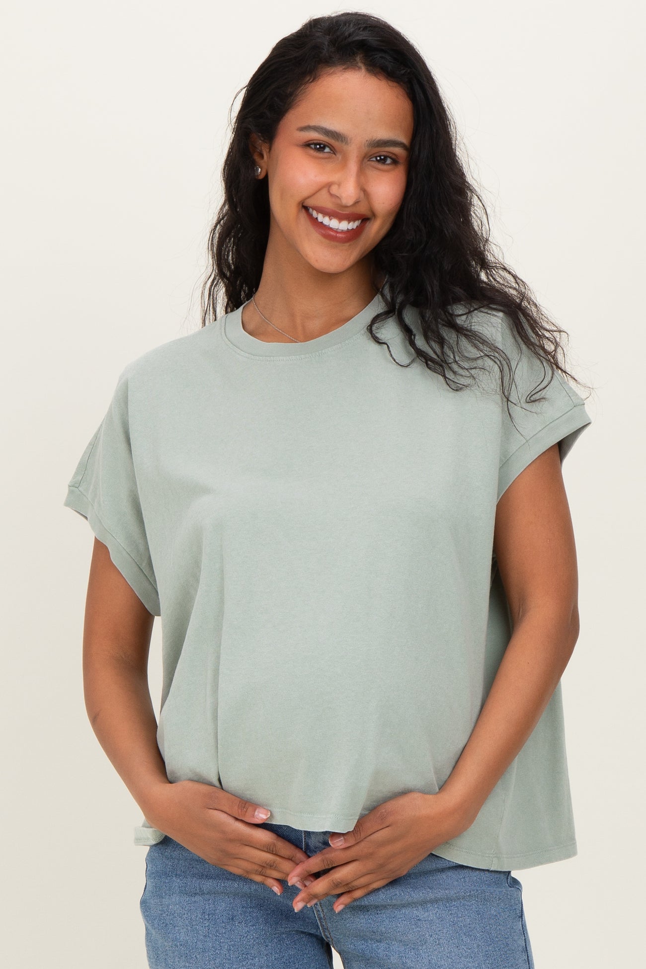 woman wearing a light green oversized maternity top and holding her baby bump