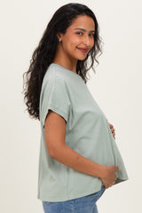 woman wearing a soft green maternity top with rolled sleeves and holding her baby bump