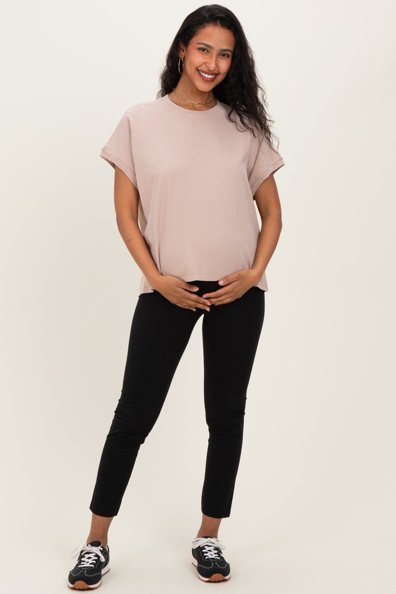 woman wearing a light pink maternity top and black pants, holding her baby bump