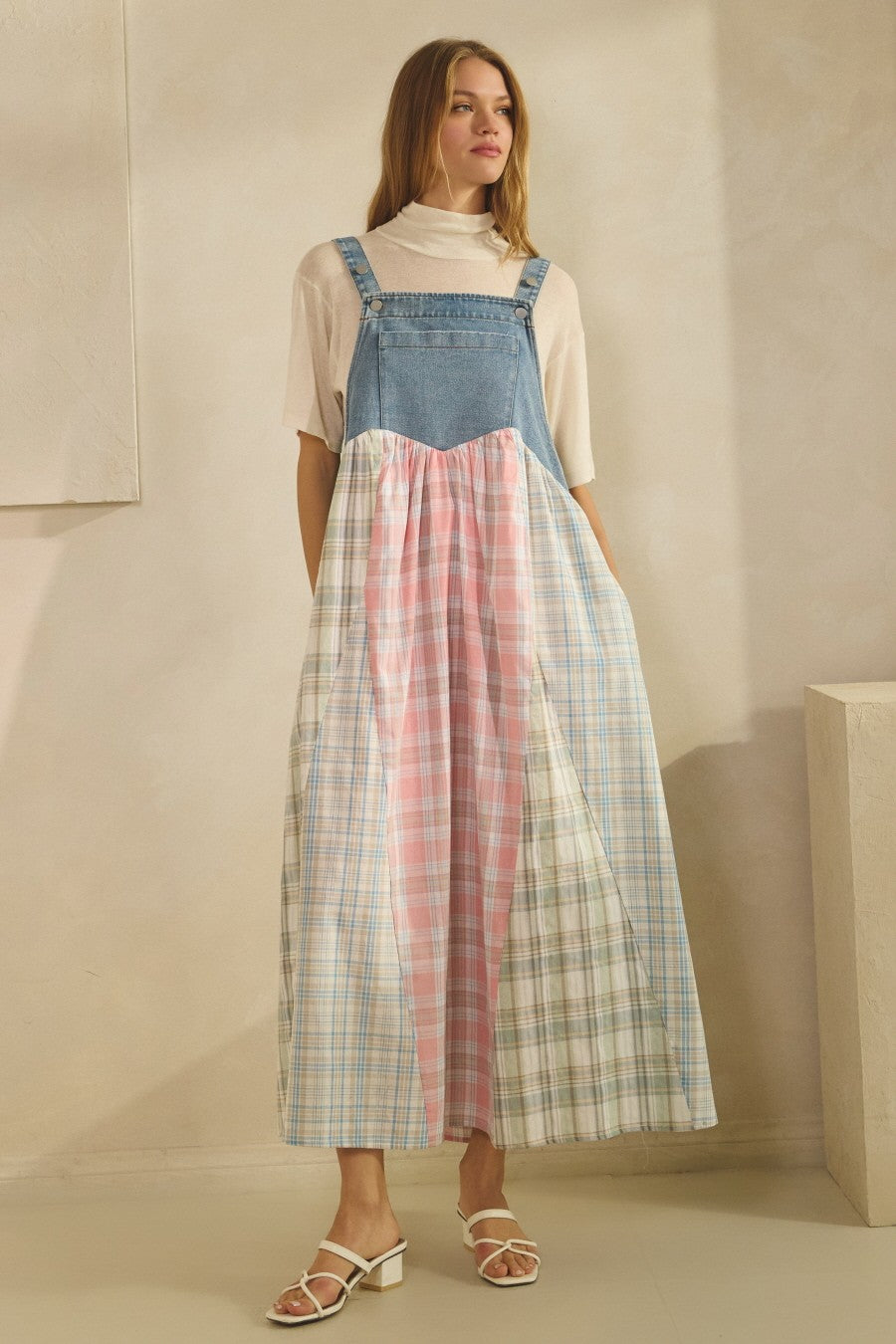 woman wearing a denim and pastel plaid color block maxi dress with a white turtleneck underneath and strappy sandals