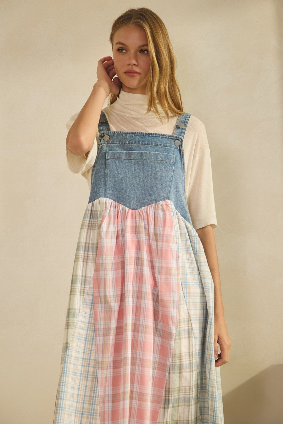 woman wearing a denim overall dress with pink and blue plaid panels over a cream turtleneck top