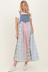 woman wearing a long plaid denim maxi dress with a white t-shirt and sneakers, standing with one hand in a pocket