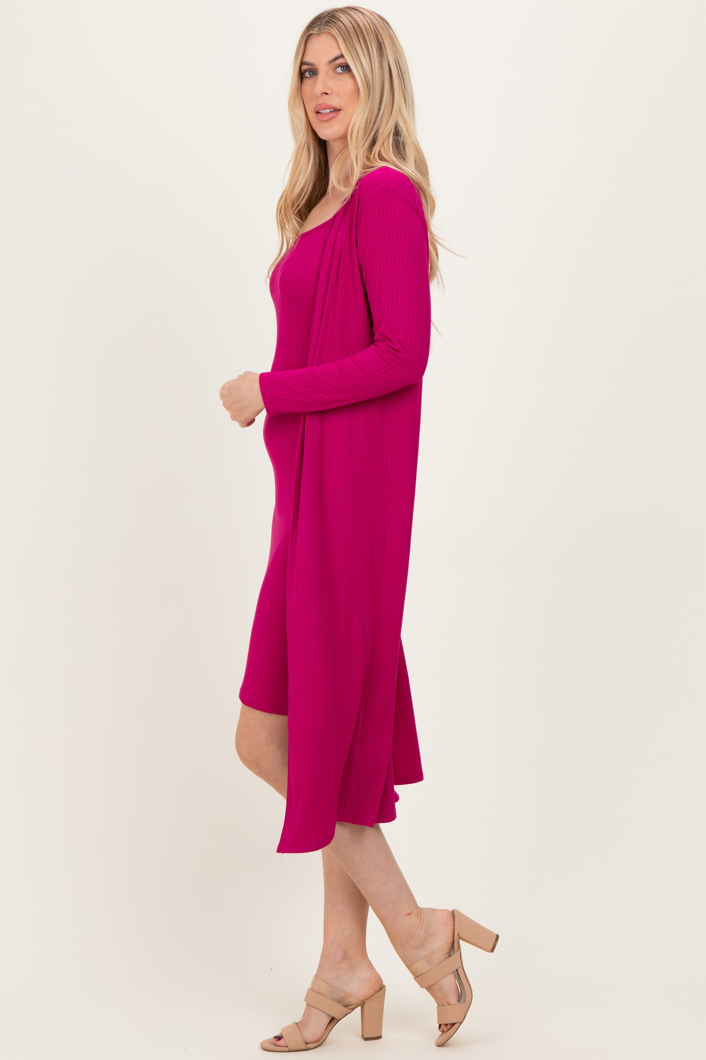 woman wearing a fuchsia ribbed dress with long sleeves and a flowing silhouette, paired with beige high-heeled sandals