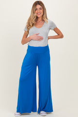 woman wearing a gray v-neck maternity top and blue wide-leg maternity pants, holding her baby bump