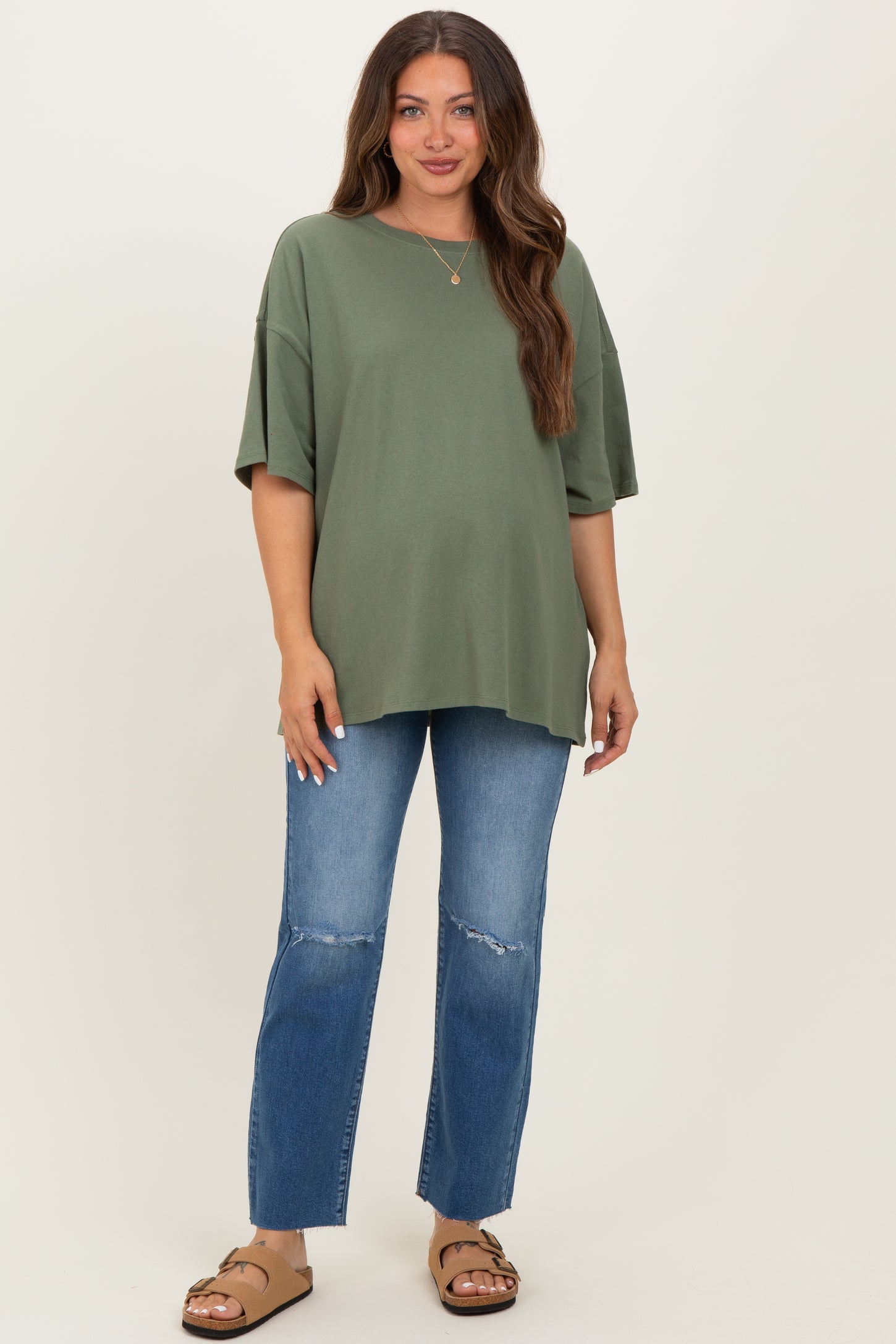 woman wearing an olive green oversized maternity top and distressed blue jeans, showing her baby bump