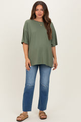 woman wearing an olive green oversized maternity top and distressed blue jeans, showing her baby bump