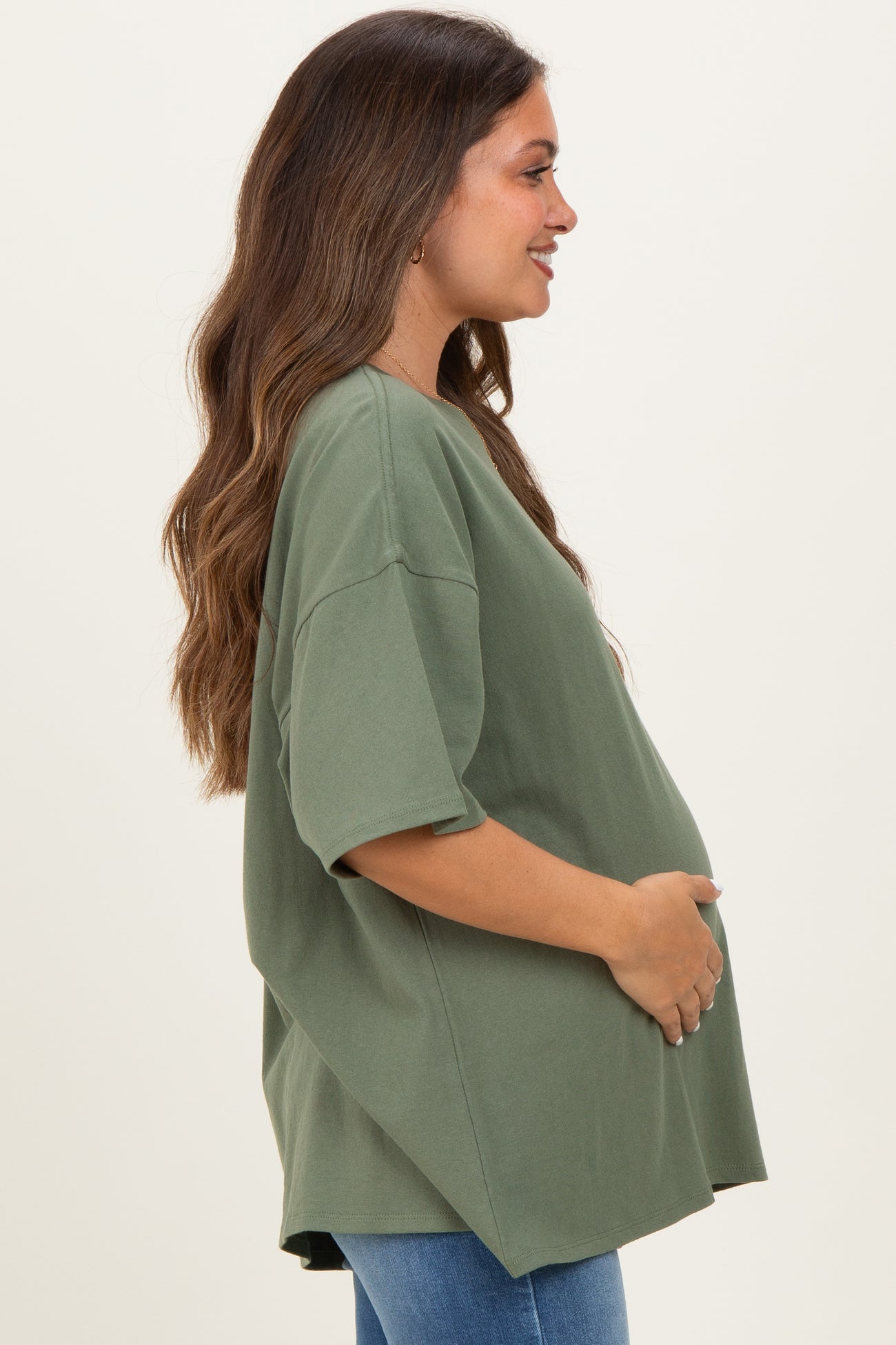 woman wearing a green oversized maternity t-shirt and gently holding her baby bump