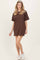 woman wearing a brown oversized t-shirt dress with short sleeves and a relaxed fit, paired with white sneakers