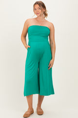 woman wearing a teal strapless maternity jumpsuit with wide legs and pockets, showing a visible baby bump