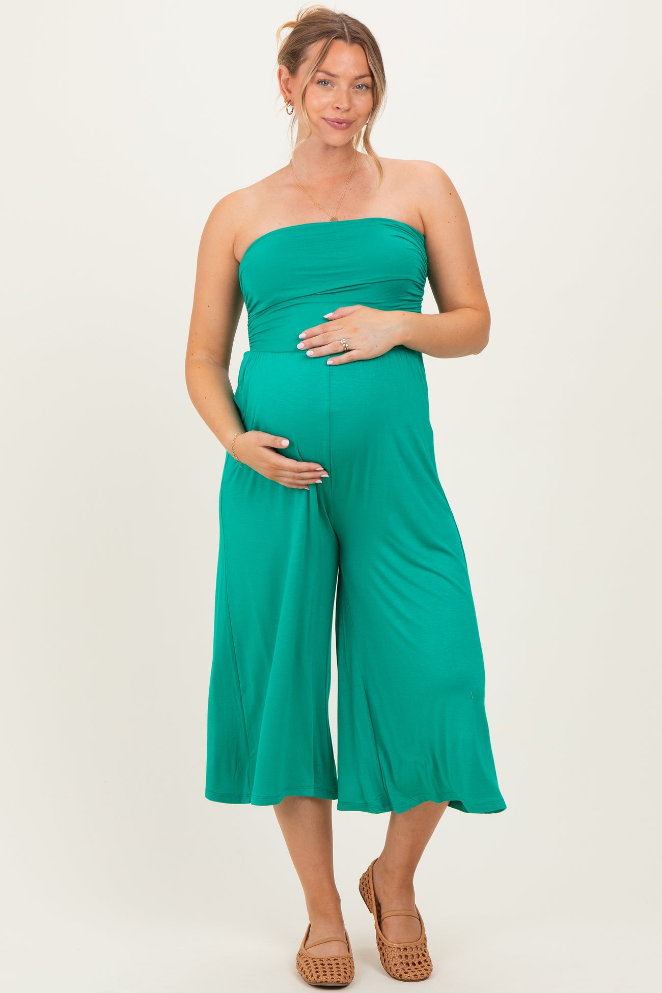 woman wearing a green strapless maternity jumpsuit and holding her baby bump