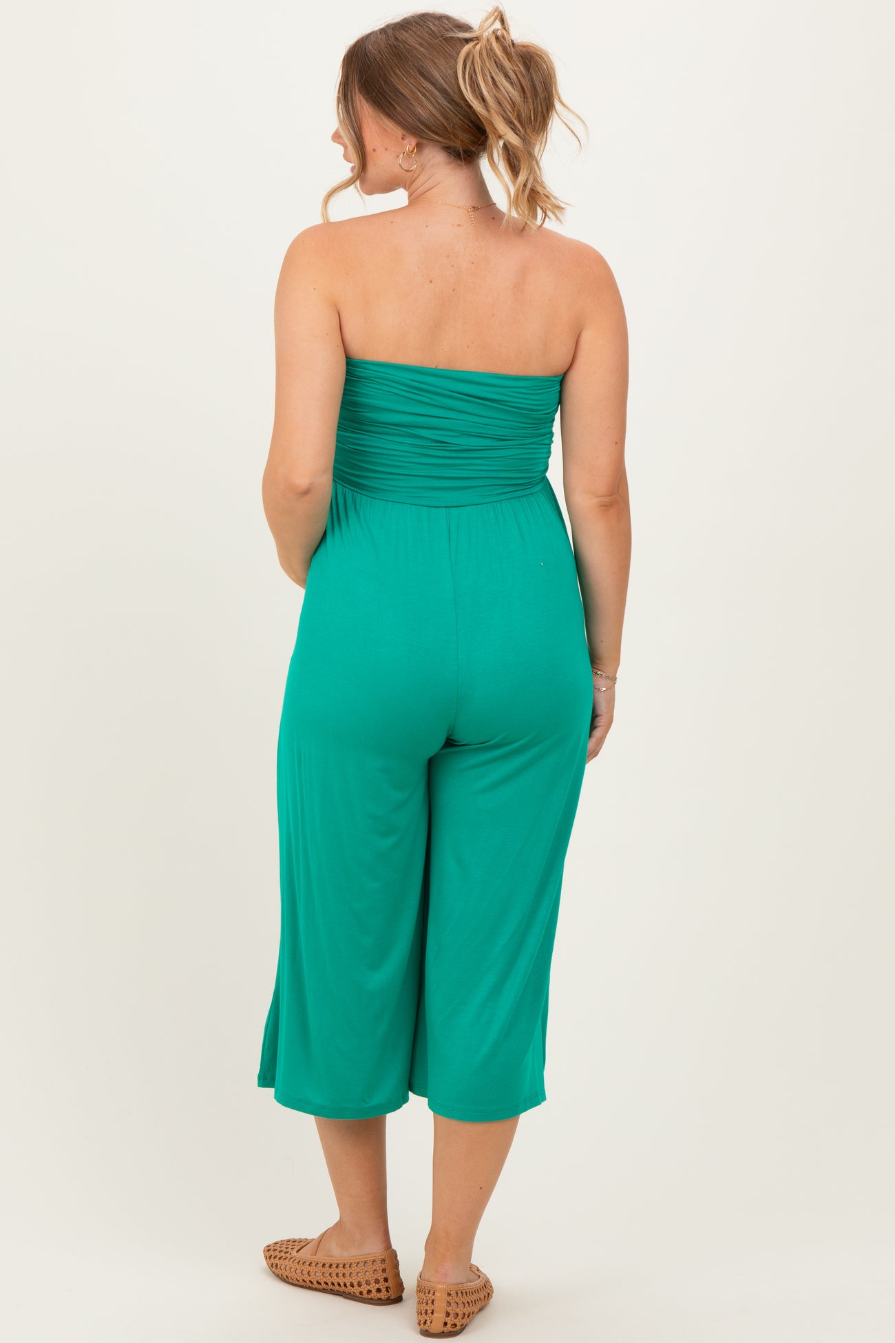 woman wearing a green strapless maternity jumpsuit with cropped legs, seen from the back