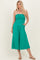 woman wearing a strapless teal jumpsuit with a ruched bodice and wide legs, posing with hands in pockets