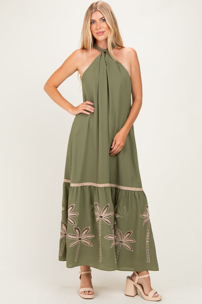 woman wearing an olive green maxi dress with halter neck and floral embroidery at the hem