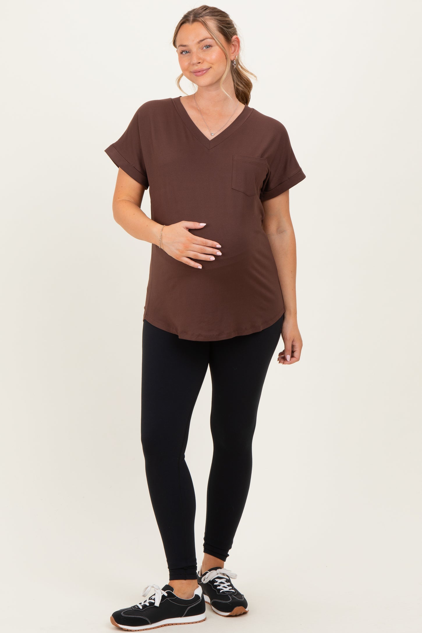 woman wearing a brown v-neck maternity top and black leggings, gently holding her baby bump