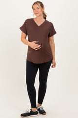 woman wearing a brown v-neck maternity top and black leggings, gently holding her baby bump