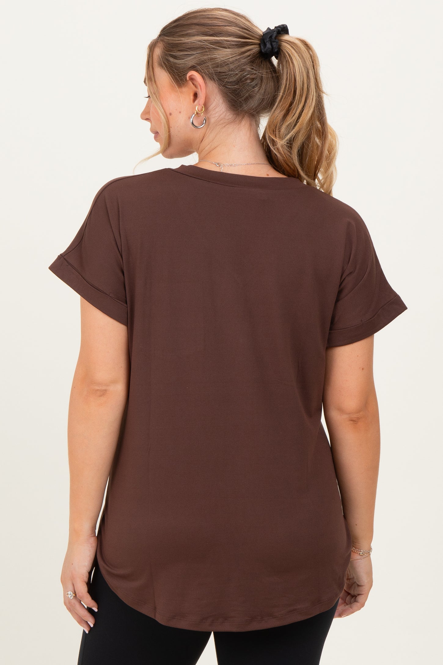woman wearing a brown short sleeve maternity top, viewed from the back, with relaxed fit and rolled sleeves