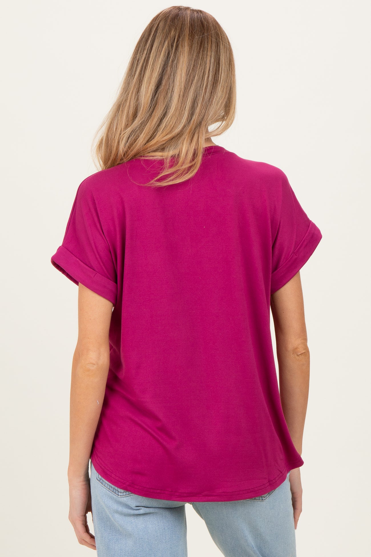 woman wearing a fuchsia short sleeve maternity top, seen from the back, with rolled sleeves and relaxed fit