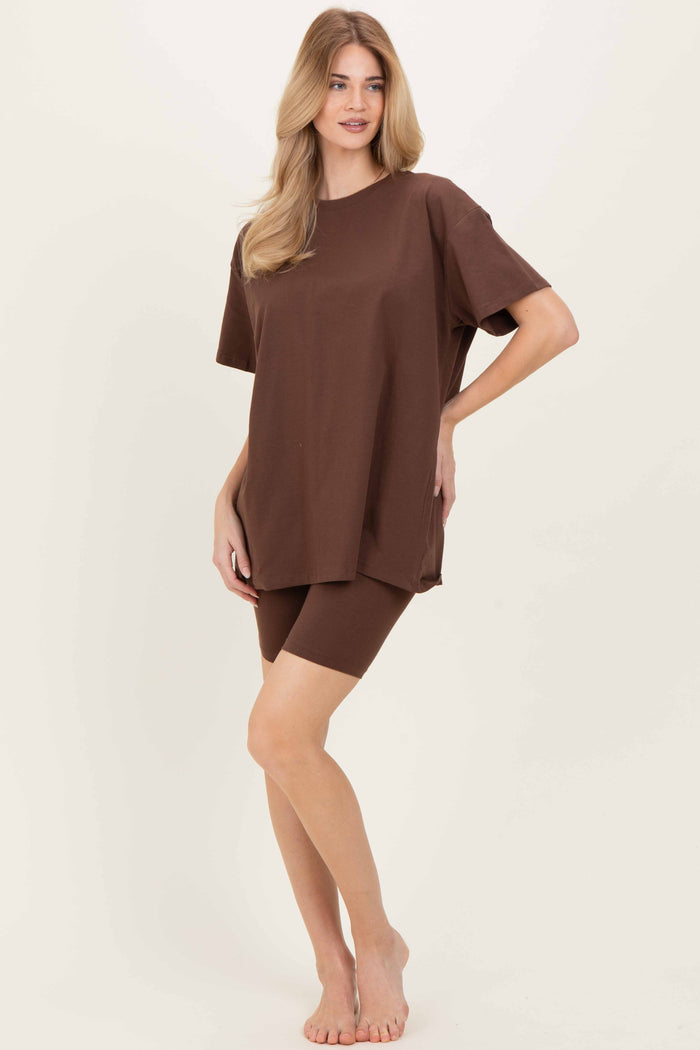 woman wearing a brown oversized t-shirt and matching knee-length shorts, standing barefoot against a light background