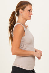 woman wearing a light beige ribbed tank top, shown from the side with long hair tied back