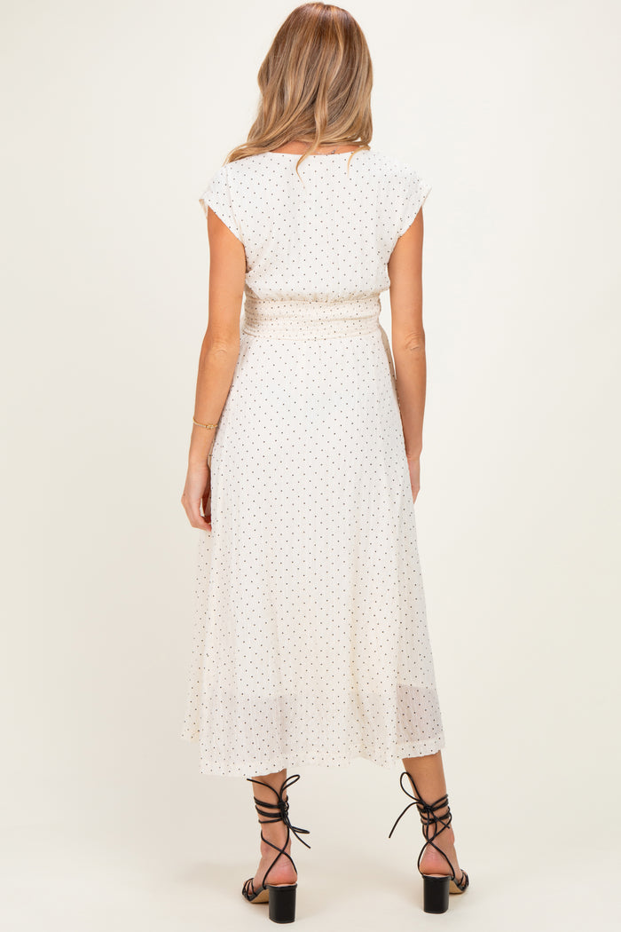 woman wearing a cream polka dot maternity dress with cap sleeves and a tie waist, viewed from the back