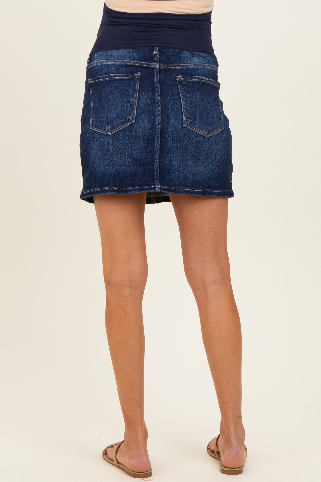 woman wearing a dark blue denim maternity skirt, showing a fitted style and mid-thigh length from the back