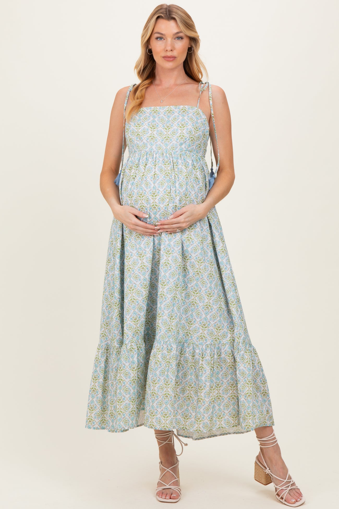 woman wearing a light blue floral maternity dress with tiered skirt and adjustable straps, holding her baby bump