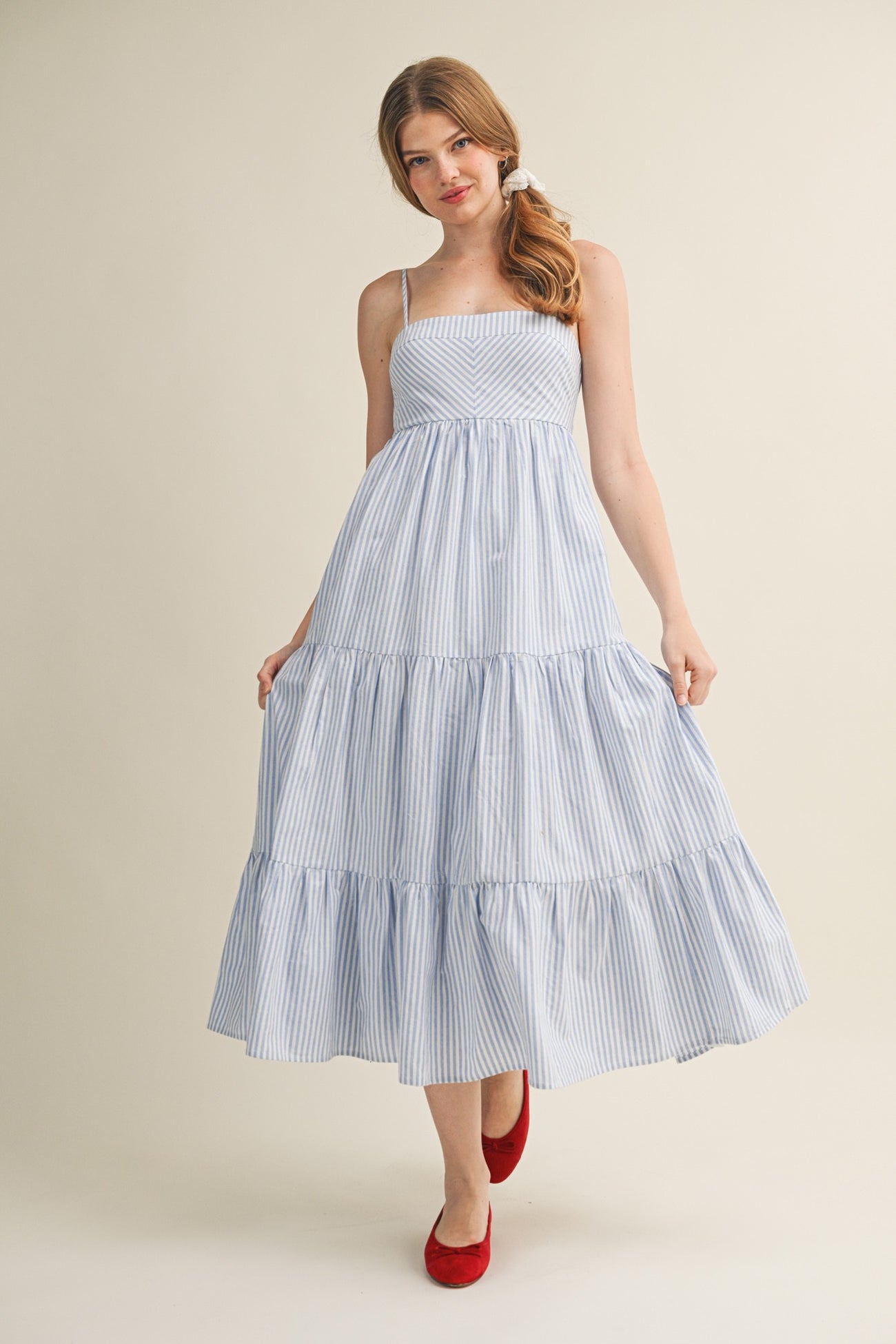 woman wearing a blue and white striped maxi dress with a tiered skirt and spaghetti straps, paired with red flats
