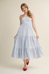 woman wearing a blue and white striped maxi dress with a tiered skirt and spaghetti straps, paired with red flats