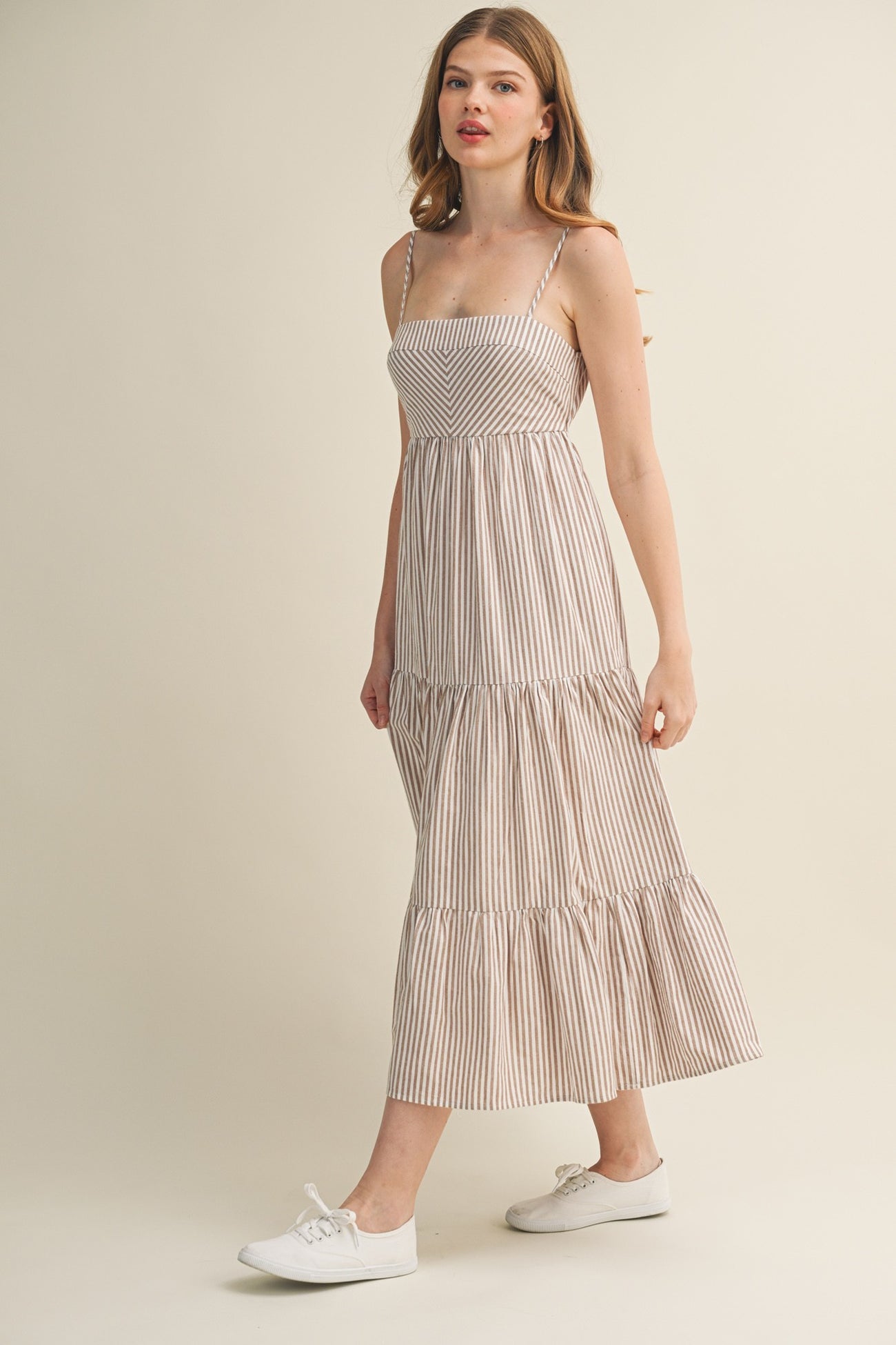 woman wearing a striped maxi dress with thin straps and tiered ruffles, paired with white sneakers