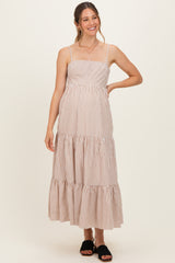 woman wearing a beige and white striped maternity maxi dress with spaghetti straps and tiered hem, smiling and standing in front of a plain background