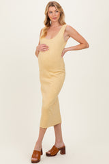 woman wearing a yellow maternity dress that highlights her baby bump, standing in a relaxed pose