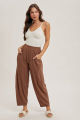 woman wearing a cream ribbed tank top and rust wide-legged pants, standing with one hand on her hip