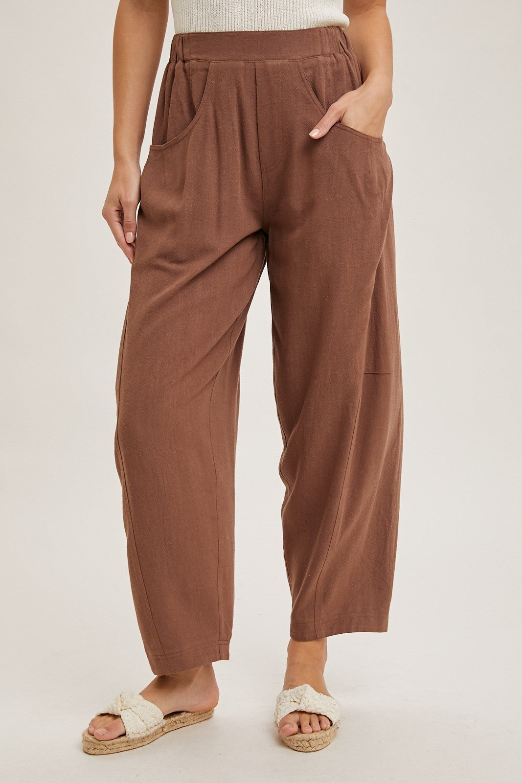 woman wearing brown pleated wide-leg pants with side pockets and a textured finish, styled with casual footwear