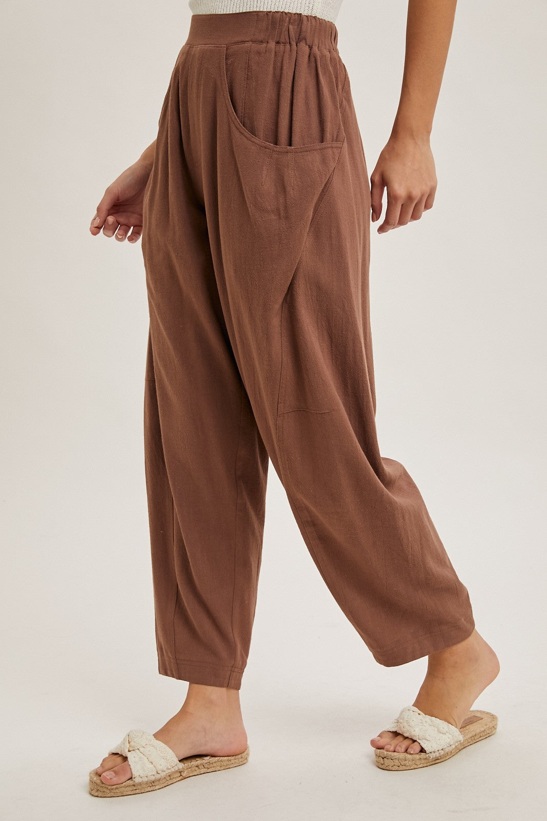 woman wearing brown relaxed-fit pants with side pockets and a high waistband, styled with slip-on sandals