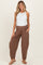 woman wearing a white tank bodysuit and brown maternity pants with pockets, standing and smiling