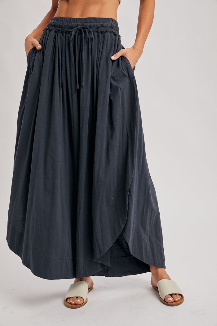 woman wearing a black maxi skirt with an elastic waistband and pockets, styled with light sandals