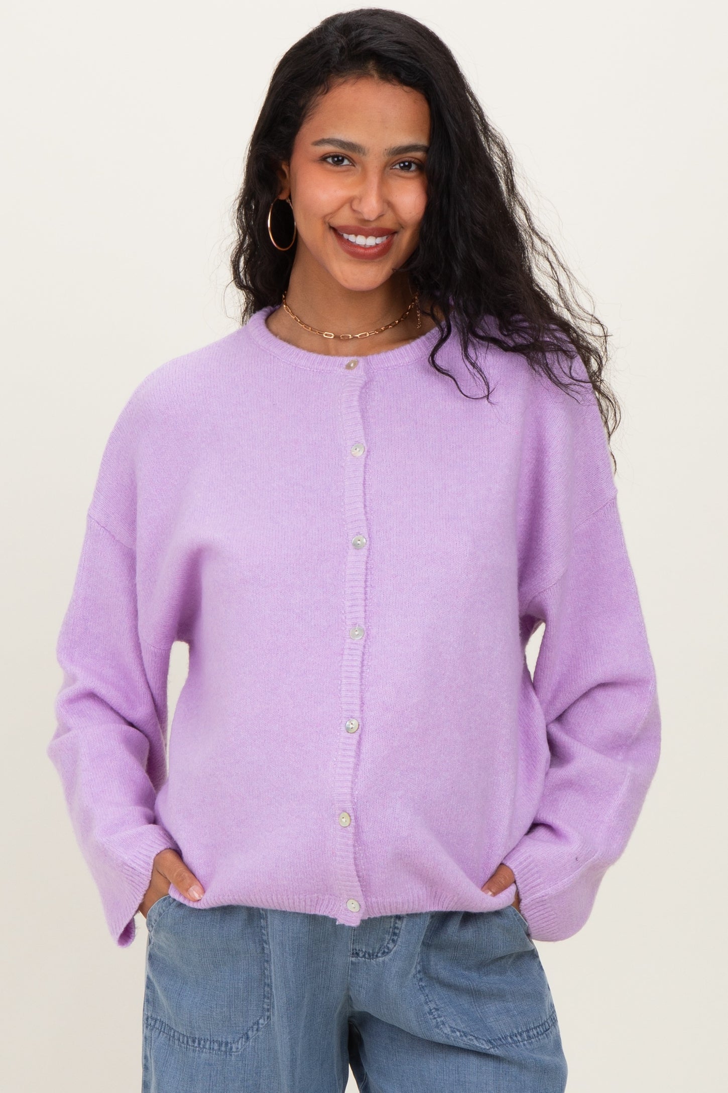 woman wearing a light purple maternity cardigan with buttons, smiling and posing with hands in pockets