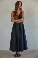 woman wearing a black and gold striped tank top and a long black skirt, standing with arms crossed