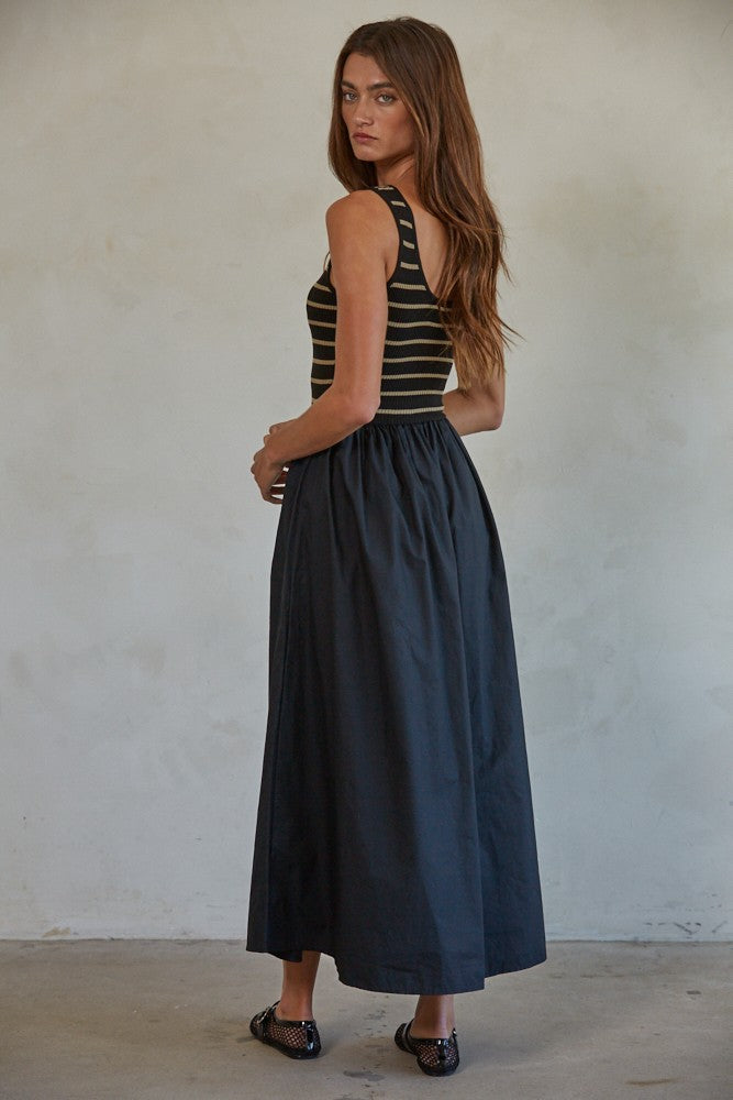 woman wearing a black and striped sleeveless maxi dress with a fitted top and full skirt, standing with her back to the camera